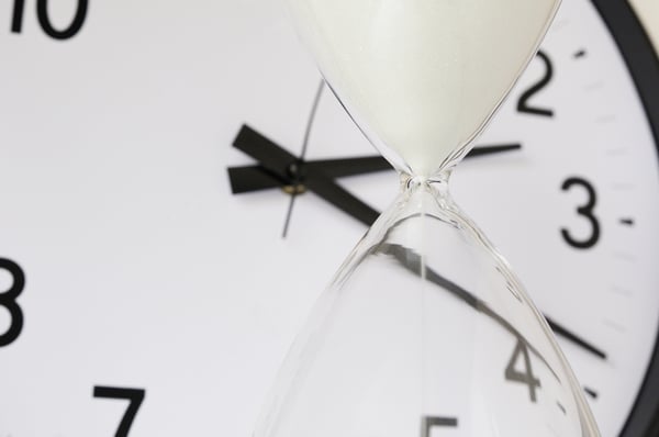 Two measurements of time White sand falling inside hourglass, with round analog clock in background